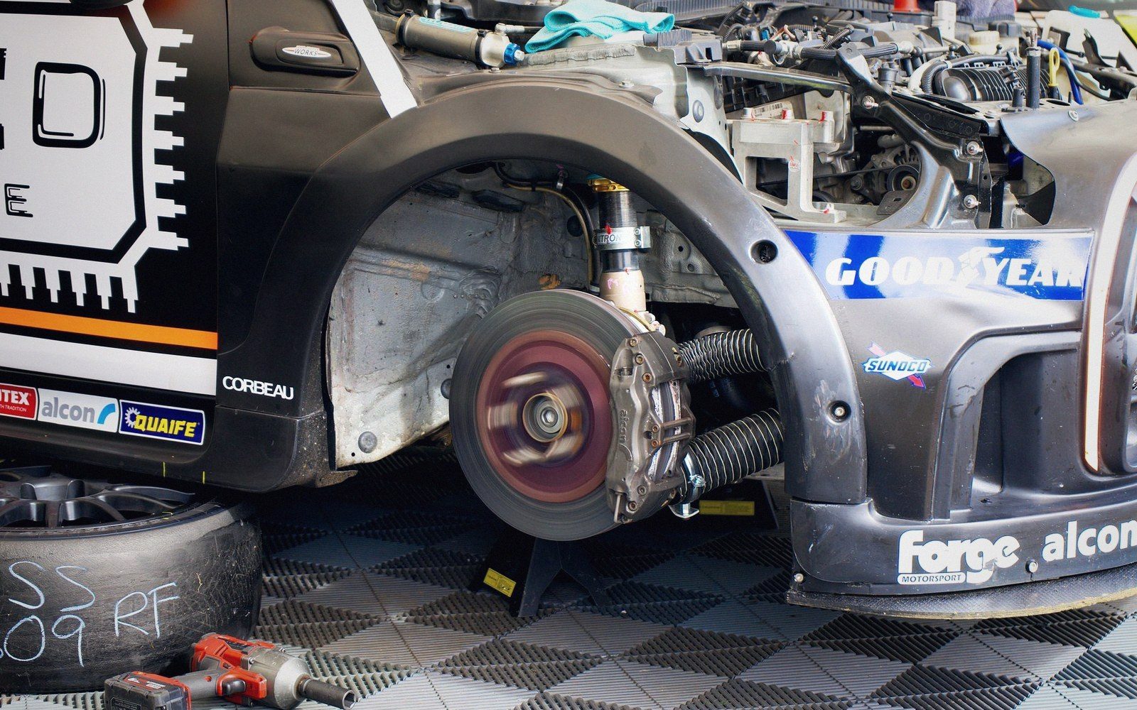 Race car with wheel removed exposing brake rotor and caliper on garage floor