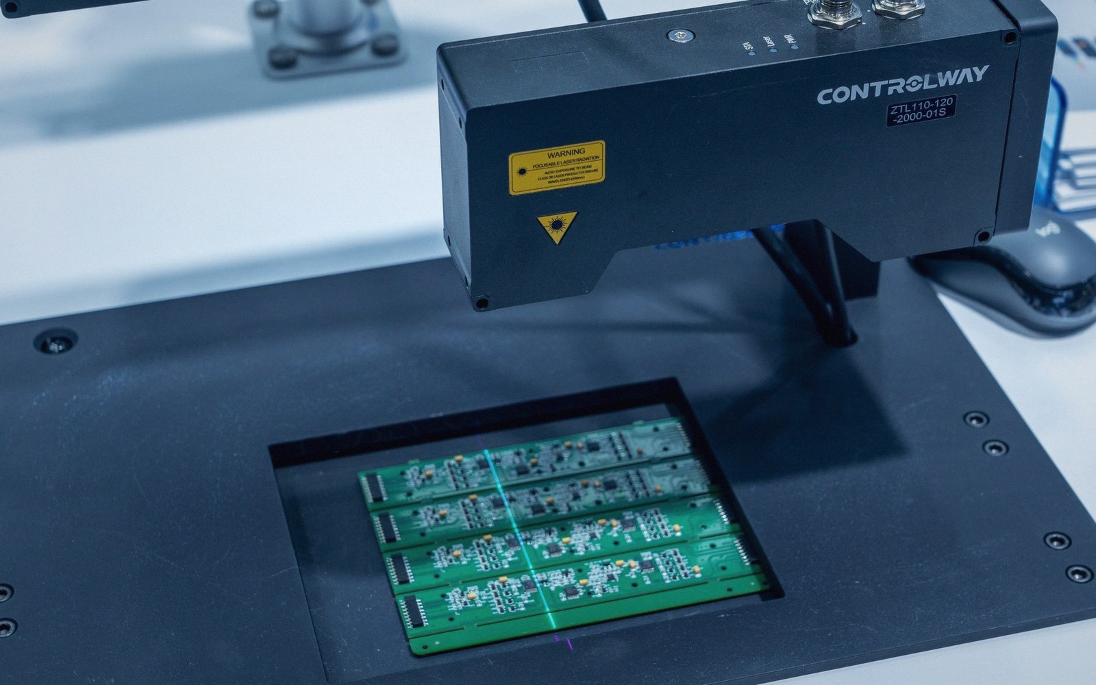 A laser marking machine positioned over green circuit boards on a workbench