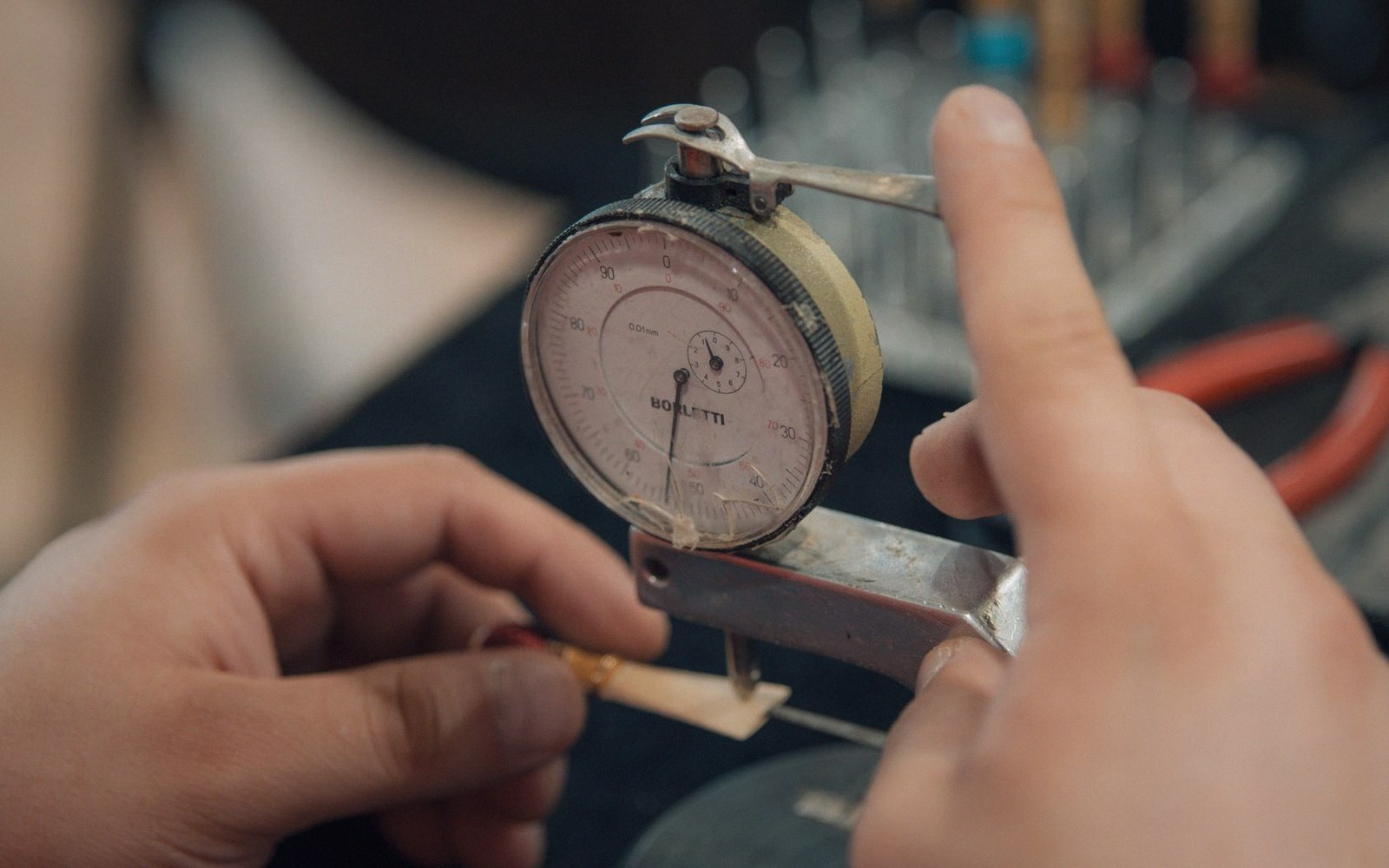 Hands using a dial thickness gauge to measure a small metal piece