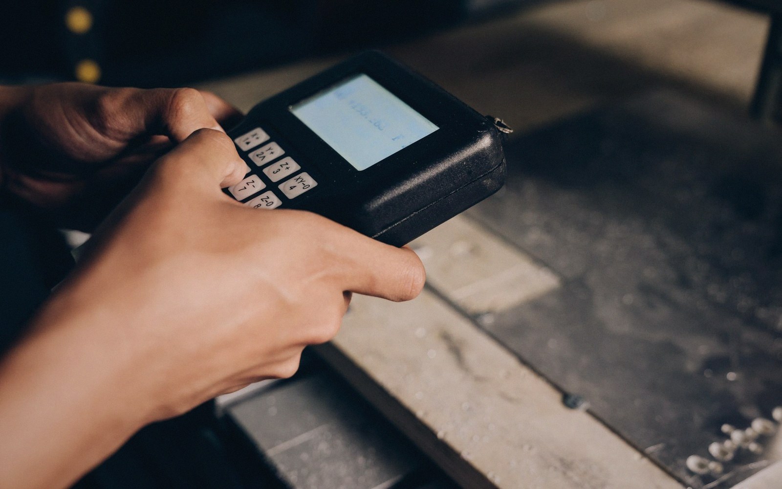 Hands entering a command on a handheld robot teach pendant with a small screen