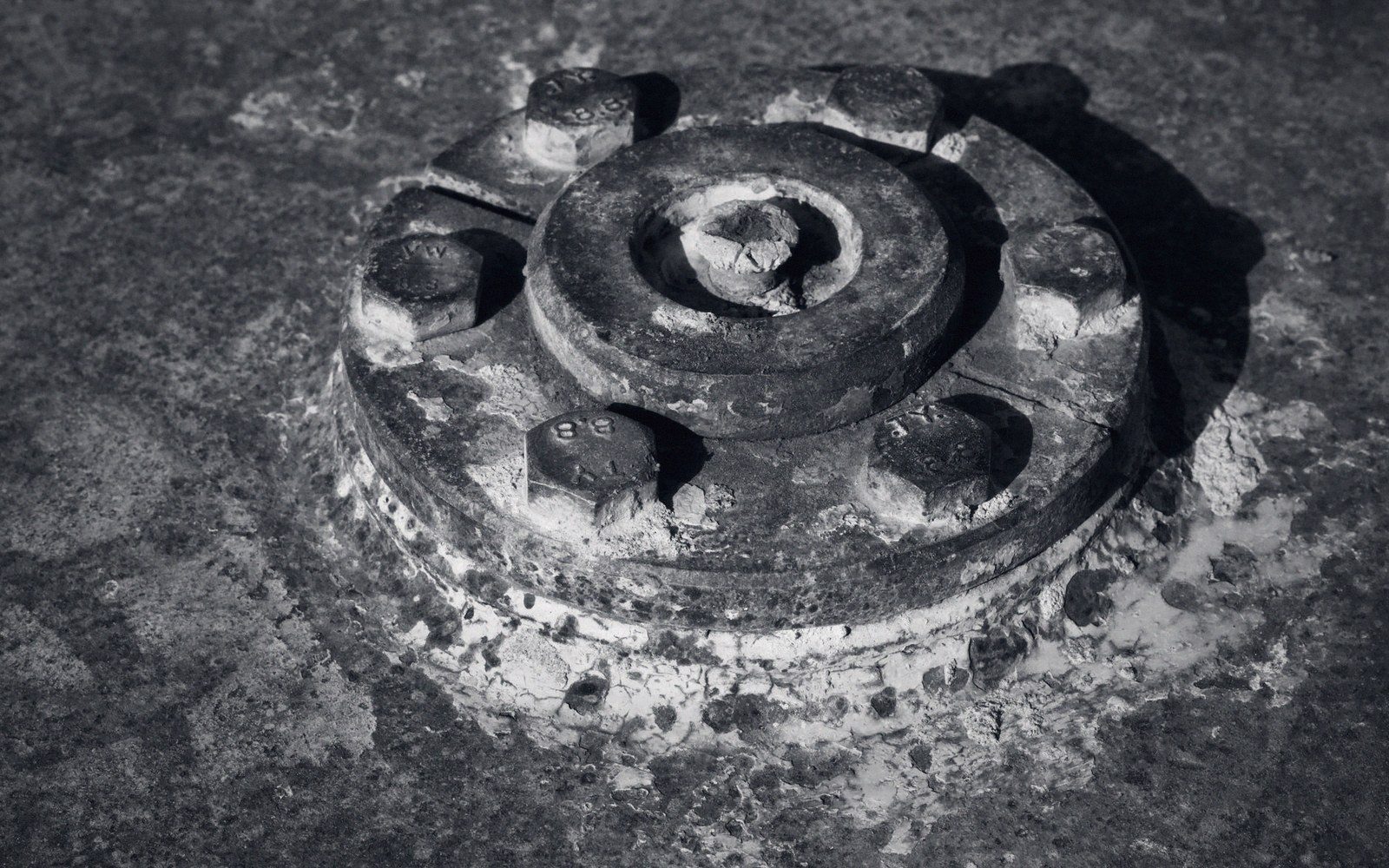 Corroded circular metal flange with six bolts embedded in a concrete floor