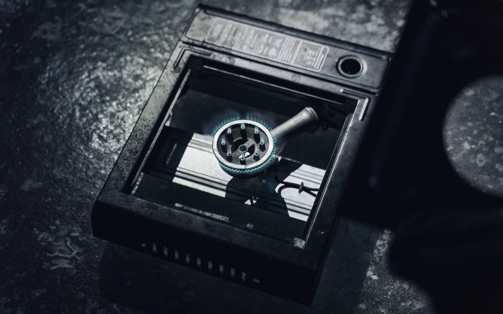 A portable gas burner glows blue-green inside its open metal casing