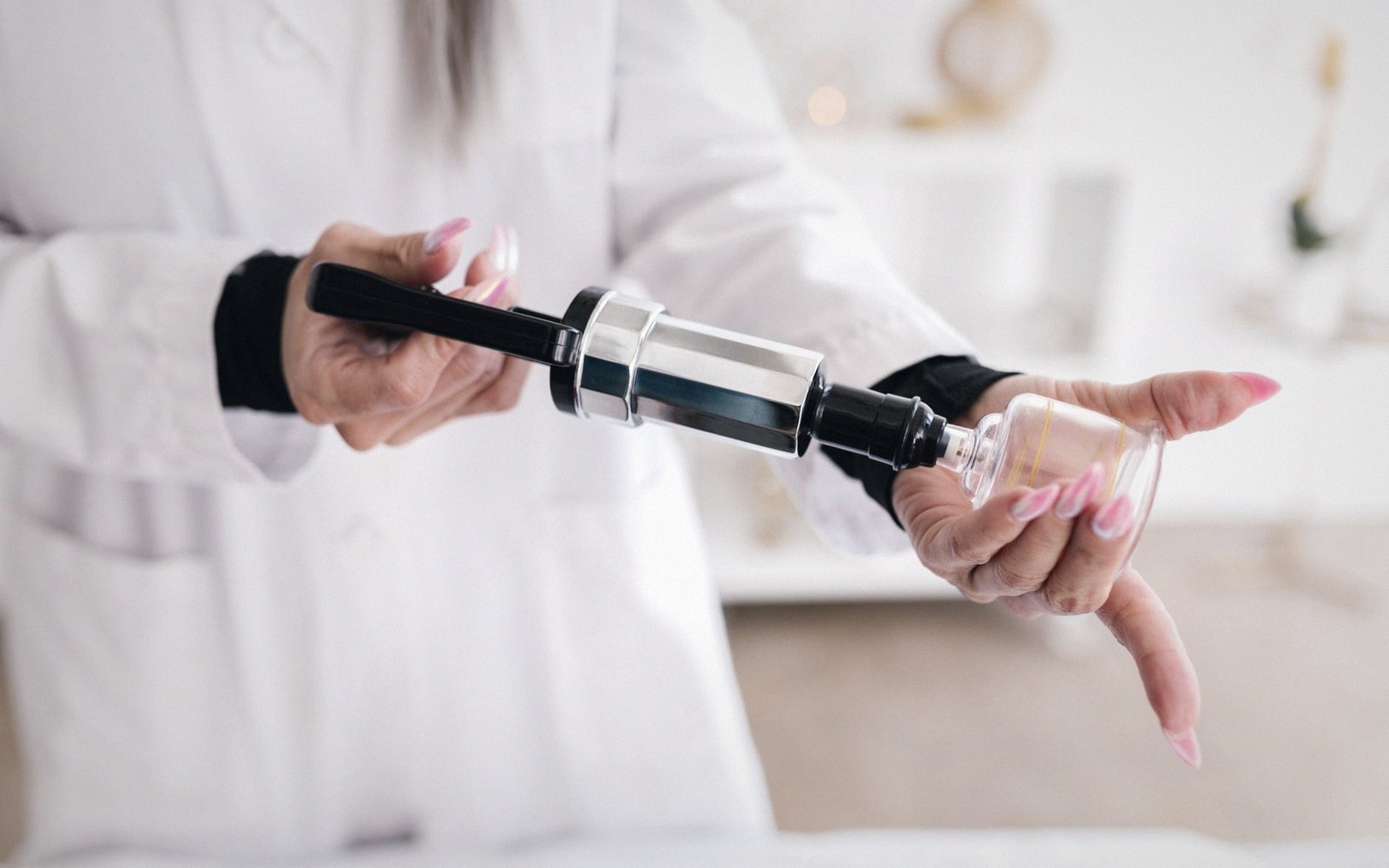 Hands in a white lab coat holding a vacuum pump device against a bottle